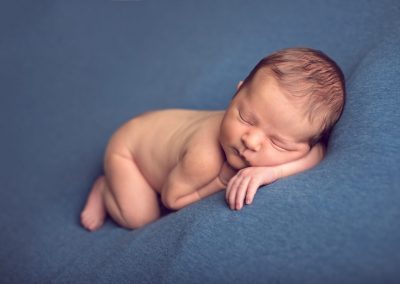 Newborn baby resting his head on his arm on blue background | newborn photography san diego | www.babiesandbeauties.com