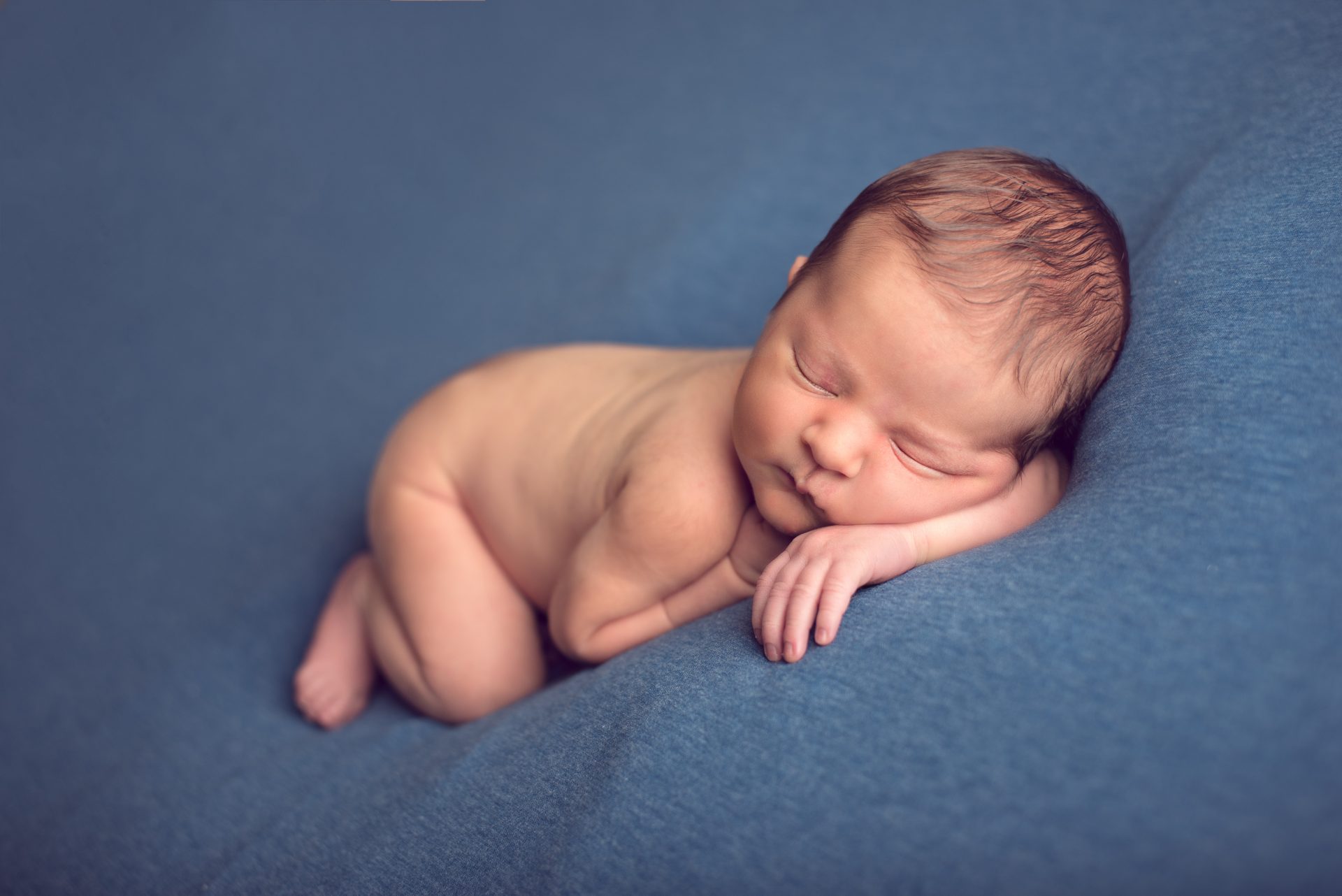 Newborn baby resting his head on his arm on blue background | newborn photography san diego | www.babiesandbeauties.com