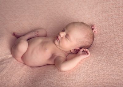 Newborn baby girl lying on back with hands in above her head | san diego newborn photography | Contact us today to book your session www.babiesandbeauties.com