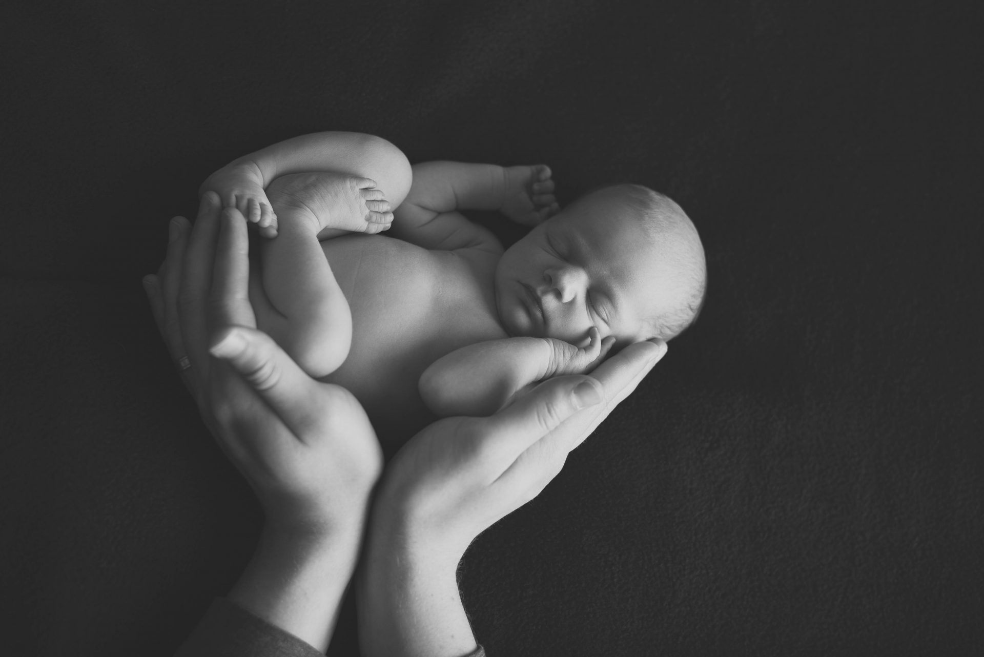 Newborn baby in dad's hands in black and white | newborn photography san diego | www.babiesandbeauties.com for more info