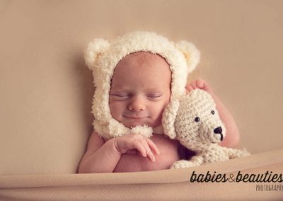 Newborn girl in cream colored bear bonnet holding stuffed bear | newborn photography san diego | Visit www.babiesandbeauties.com to learn more!
