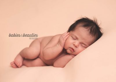 Newborn girl lying with hands on cheeks on pink background | san diego newborn photography | Visit www.babiesandbeauties.com to learn more!