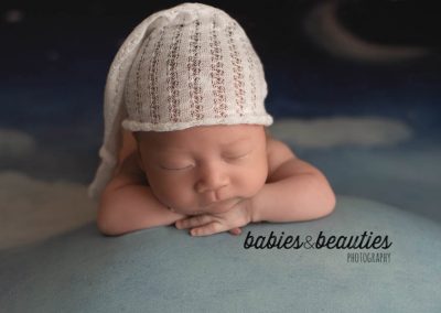 Newborn baby in white night cap with clouds and moon in background | Newborn photos san diego | Visit www.babiesandbeauties.com