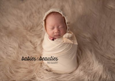 newborn baby in cream wrap and headband on cream fur | baby photography san diego | Visit www.babiesandbeauties.com