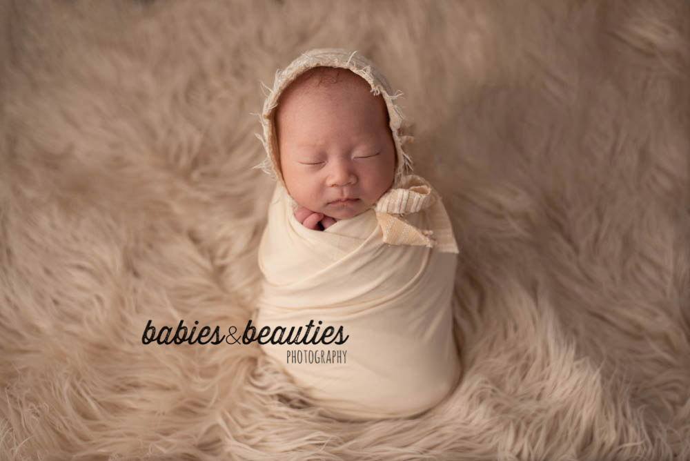 newborn baby in cream wrap and headband on cream fur | baby photography san diego | Visit www.babiesandbeauties.com
