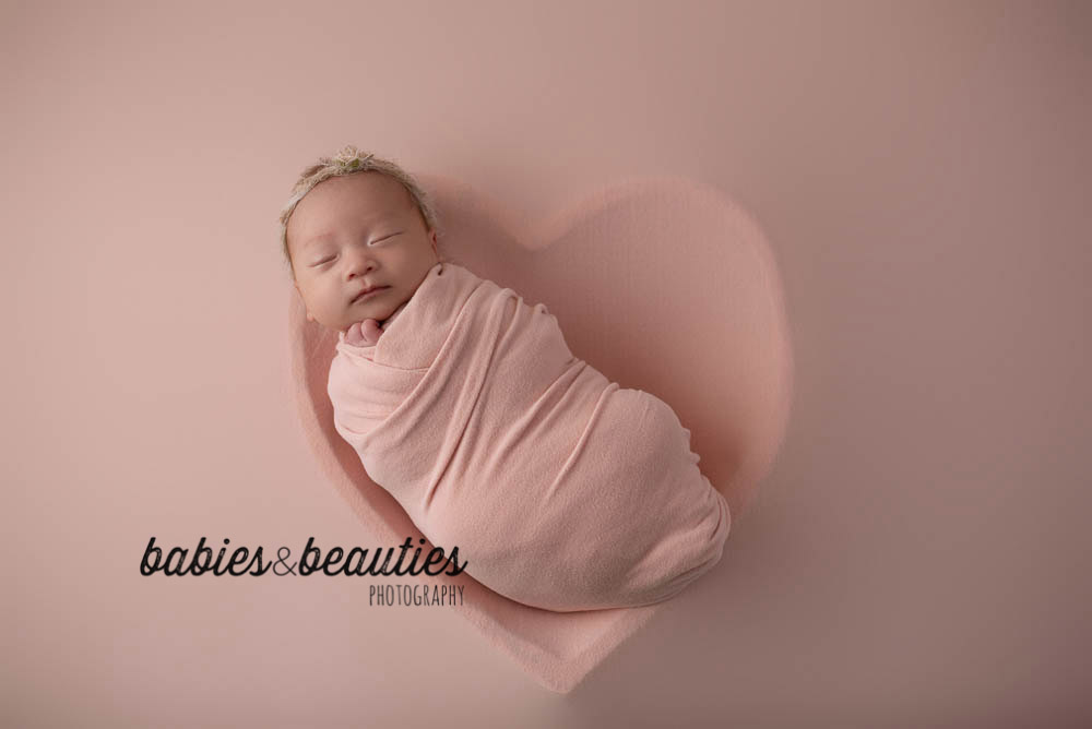 Newborn baby girl in pink in heart shaped bowl | san diego newborn photography | Visit www.babiesandbeauties.com