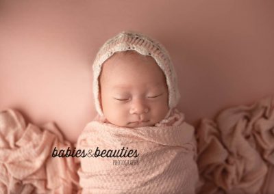 Newborn photo of baby girl wrapped in pink with pink and cream lace bonnet | Newborn photos san diego | www.babiesandbeauties.com