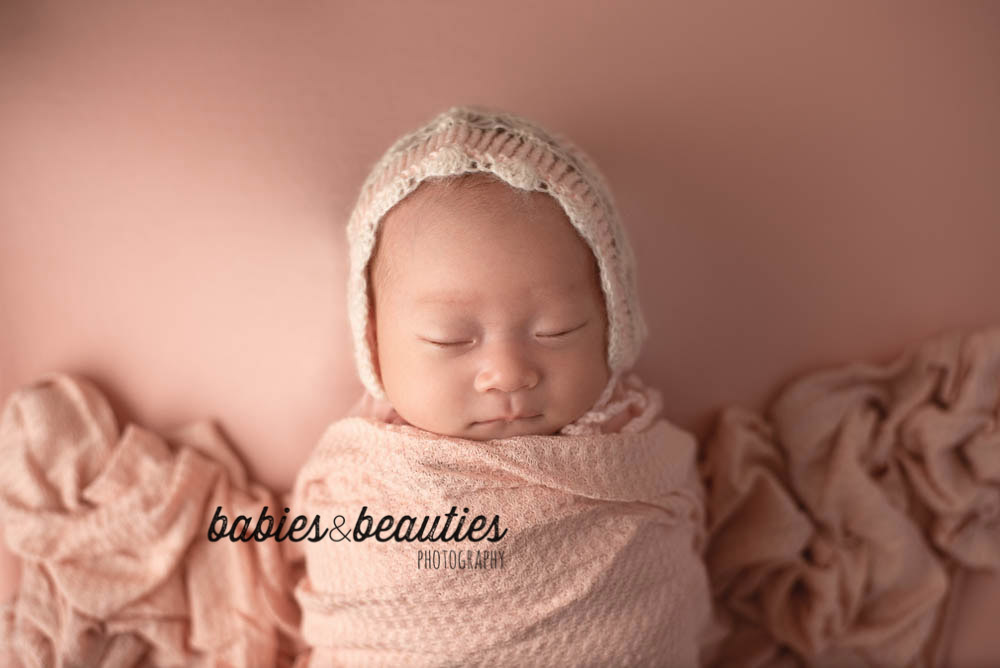 Newborn photo of baby girl wrapped in pink with pink and cream lace bonnet | Newborn photos san diego | www.babiesandbeauties.com