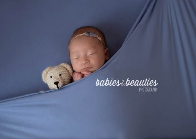 Newborn girl in headband with a tiny periwinkle bow next to a stuffed bear | newborn photos san diego | Visit www.babiesandbeauties.com