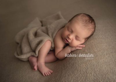 Newborn baby on tan backdrop with cheek on hand | newborn photos san diego | Visit www.babiesandbeauties.com to learn more!