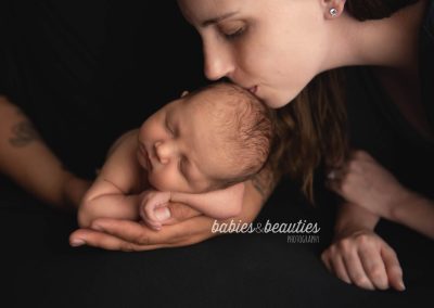 Mom kissing newborn baby's head while baby sleeps in dad's hands | San Diego newborn photographers | Visit www.babiesandbeauties.com to learn more!