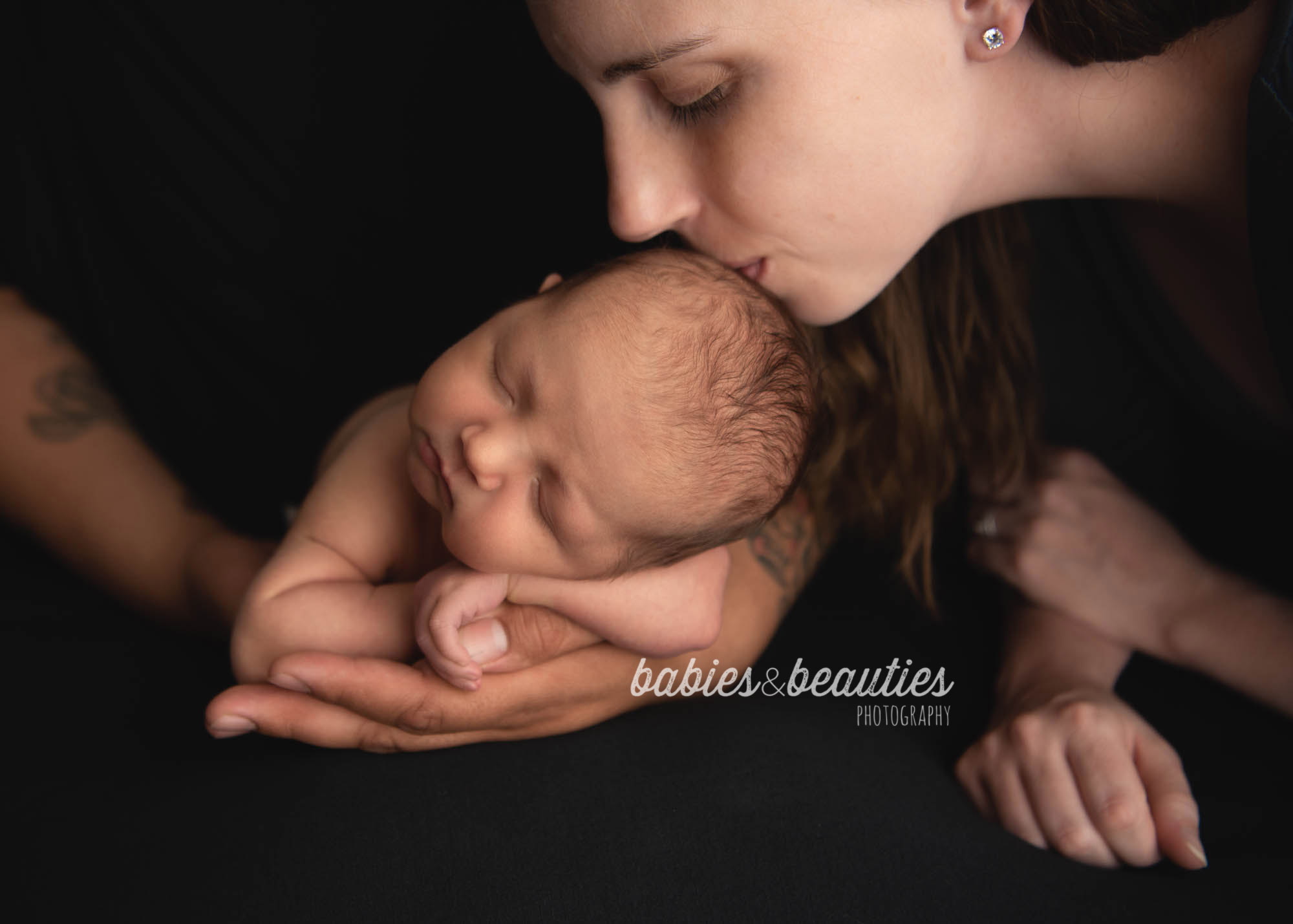 Mom kissing newborn baby's head while baby sleeps in dad's hands | newborn photography in san diego | Visit www.babiesandbeauties.com to learn more!