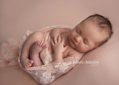 Newborn girl in lace wrap on pink backdrop | newborn photos san diego | Visit www.babiesandbeauties.com to learn more!