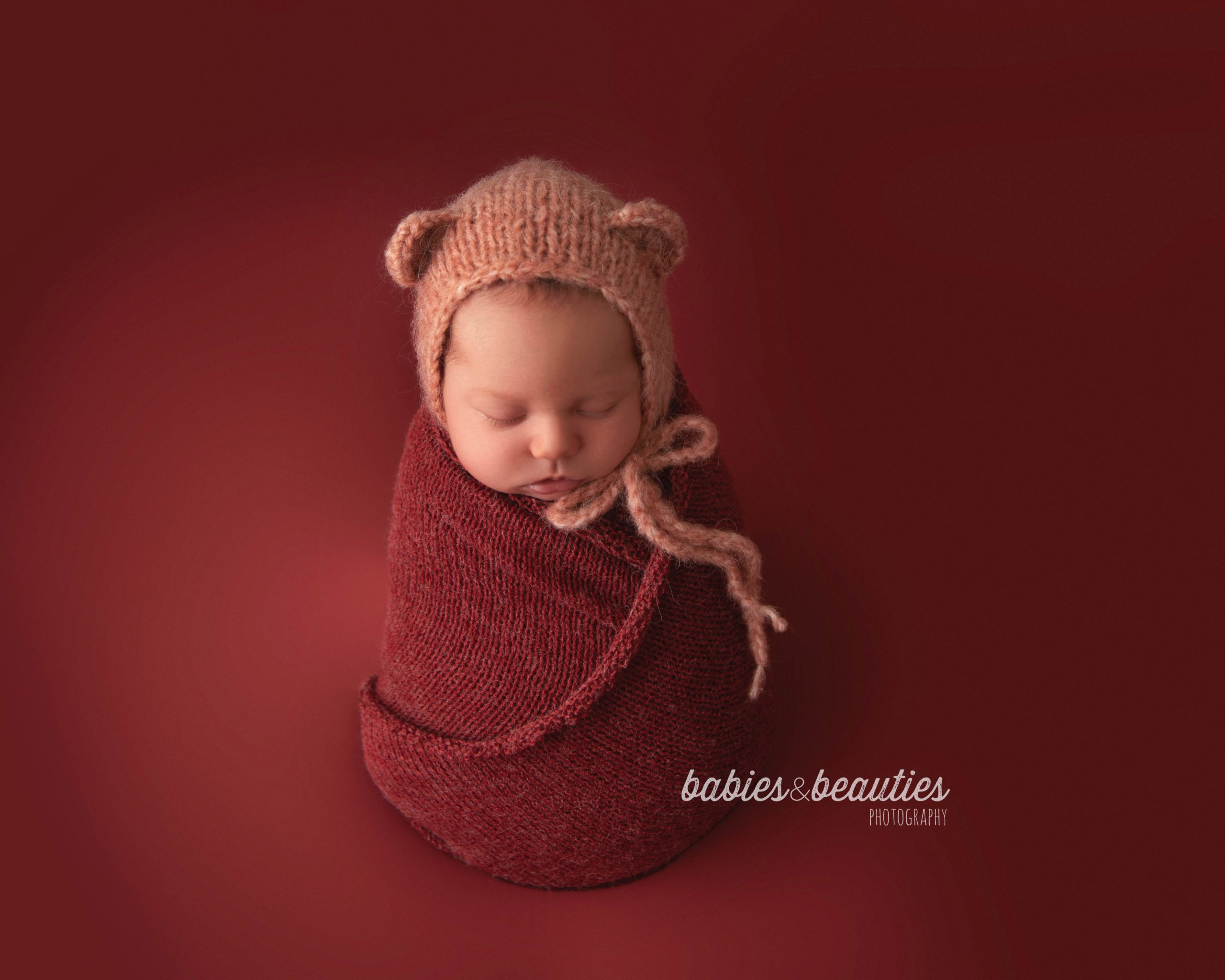 Newborn girl in bear bonnet on red backdrop | newborn photography san diego | Visit www.babiesandbeauties.com to learn more!