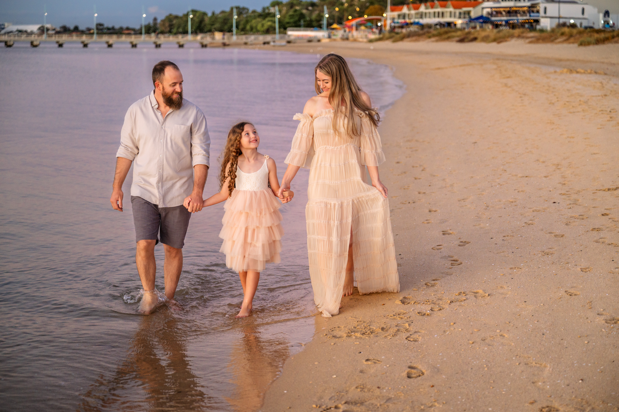 Family in coordinating outfits walks down beach during a family photoshoot.