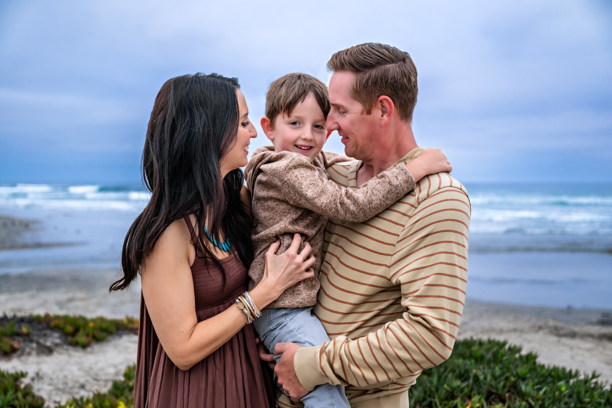 Parents snuggle their son at Oceanside Beach during a family photo session.